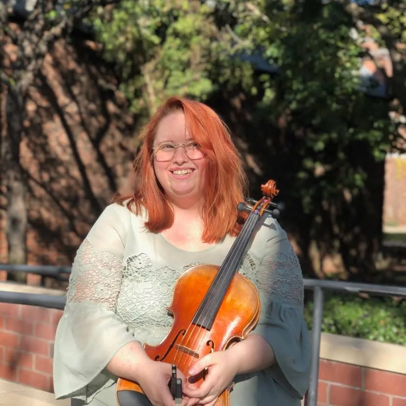 Emily Gasper with her viola outdoors in warm afternoon light.